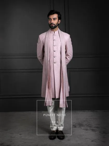 Blush tones meet timeless artistry. A sherwani in pink silk, layered with a fish-scale textured achkan and matching stole, becomes a portrait of soft elegance.