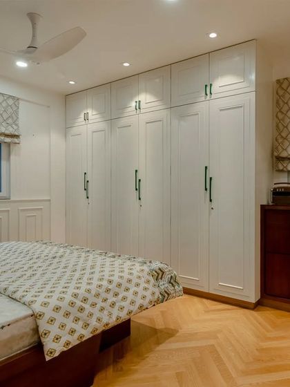 This bedroom showcases a clean, symmetrical design with a custom wardrobe in white and a chest of drawers in polished wood, tied together with green handles.