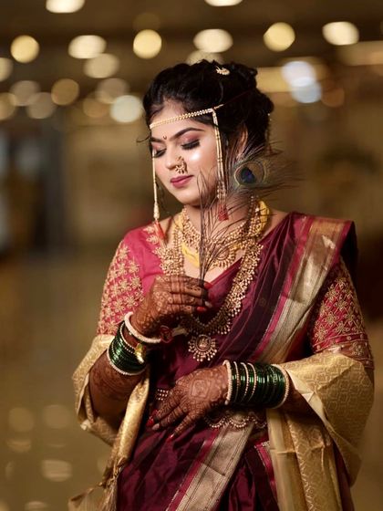 A serene portrait of a bride in a deep maroon saree. The peacock feather adds a symbolic and artistic touch to the traditional look.