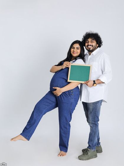 A fun and classic studio portrait of an expecting couple. They hold a blank chalkboard, perfect for adding a personalized message or due date announcement.