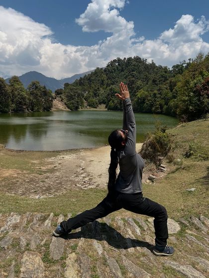 Practicing Virabhadrasana I by the tranquil waters of Deoria Tal, with the mountains reflecting in the lake. This pose helps me feel grounded and strong, drawing energy from the earth beneath my feet.