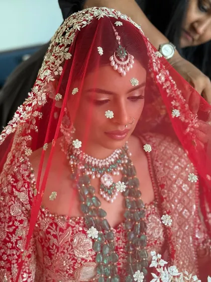 The magic of the veil. This shot captures the bride under her red net dupatta, with the makeup subtly glowing through. It’s a testament to creating a look that is both delicate and impactful.