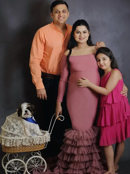 A full family portrait from a maternity session, showcasing the expecting mother, father, daughter, and their cute dog in a vintage-style pram.