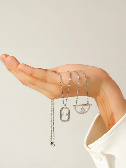 A close-up of a hand holding three distinct silver necklaces against a clean background. This shot effectively displays multiple products at once, allowing customers to compare styles.