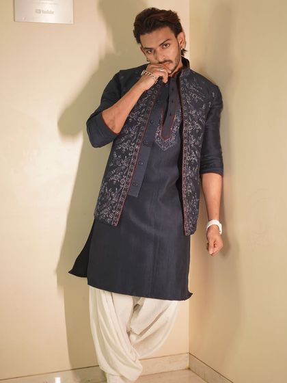 Influencer Shadab Khan showcases a contemporary look with this dark navy kurta and embroidered jacket set. Paired with traditional dhoti-style pants, it's a bold fusion of styles.