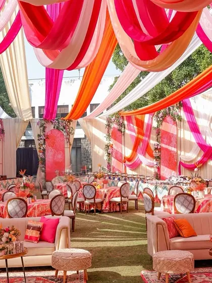 A vibrant Mehendi setup with a canopy of flowing drapes in shades of pink, orange, and white, creating a joyful and colorful atmosphere for the celebration.