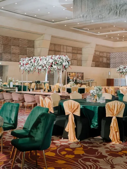 The dining setup for the moody luxe theme, featuring emerald green velvet chairs, contrasting peach bows, and tall floral centerpieces, creating a rich and elegant tablescape.