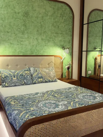 This master bedroom combines a pastel green accent wall with a beautiful cane and wood bed frame. The mirrored wardrobe doors enhance the sense of space, while the overall design creates a cozy and relaxing sanctuary.