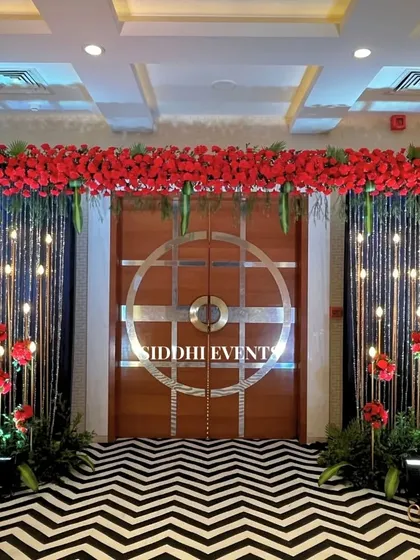 A dramatic entrance with a bold black and white chevron carpet, a canopy of red flowers, and sparkling string lights, perfect for a glamorous evening affair.