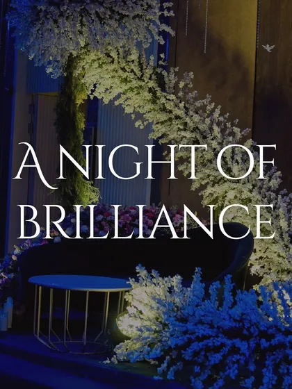 A video titled "A Night of Brilliance," showcasing a Sangeet with a stunning white floral backdrop and deep blue ambient lighting.
