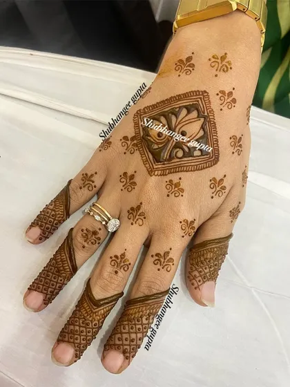 A very minimal and modern design. The central lotus motif is surrounded by tiny dots, and the fingers have simple, elegant patterns.