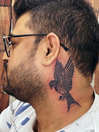 A swallow bird tattoo behind the ear and on the neck. Swallows are symbols of travel, loyalty, and freedom. This placement is bold and makes a definite statement.
