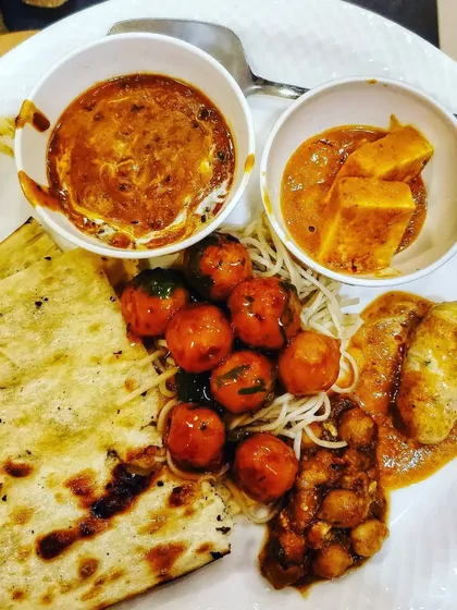 A plate showcasing the variety we offer, including noodles with manchurian, paneer butter masala, and naan.