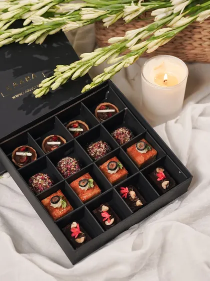 Our Rakhi Re-Imagined Box features sixteen handcrafted modern Indian sweet bites. This elegant gift box includes a delightful assortment of White Chocolate & Almond Cake, Cherry & Milk Chocolate Tarts, and our wholesome Roasted Almond & Whole Wheat Ladoos, perfect for sharing sweet moments.