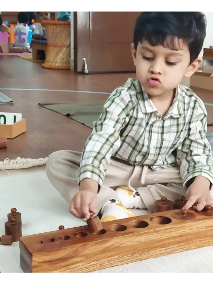 A child shows deep concentration while working with the Montessori knobbed cylinder block. This sensorial activity helps refine his visual discrimination of size and prepares him for writing by strengthening his pincer grip.