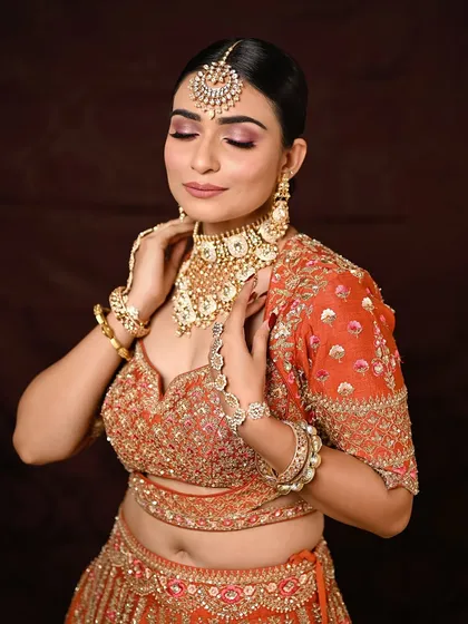 A moment of serenity. With her eyes closed, you can fully appreciate the beautiful blend of pink and rose gold eyeshadow, a perfect choice for a modern bride wearing a vibrant orange lehenga.