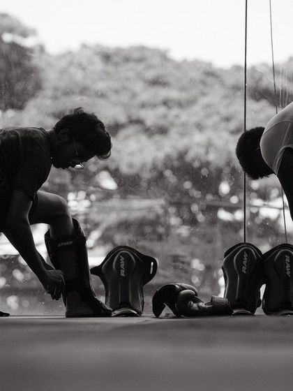 The preparation is part of the ritual. Two young fighters gear up with shin guards before a sparring session, a critical step for ensuring safety on the mats.