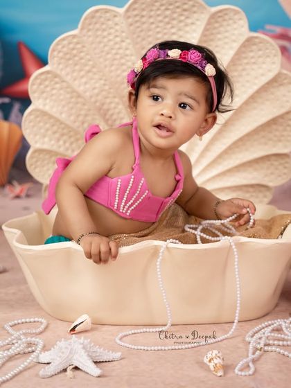 A close-up of the baby girl in her mermaid costume, playing with a string of pearls in our custom-designed "under the sea" set.