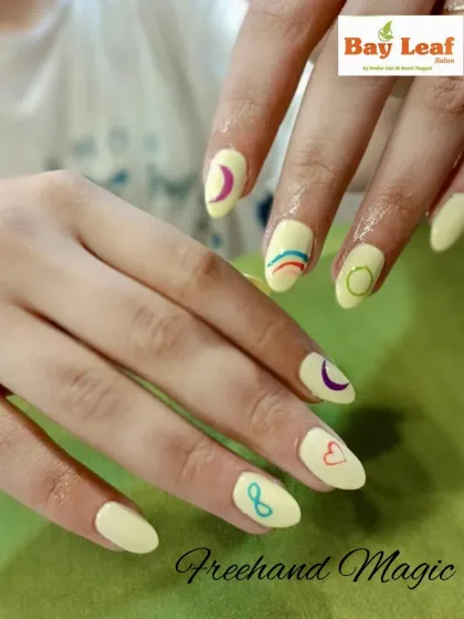 A touch of freehand magic. These nails feature a soft yellow base with minimalist, colorful symbols like a heart, crescent moon, and infinity sign for a personalized touch.