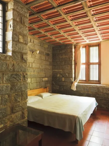 A bedroom in Mr. Petachi's house, with walls of exposed local stone and a ceiling of filler slabs using terracotta tiles. These natural, heavy materials provide excellent thermal mass, keeping the room cool and comfortable year-round.