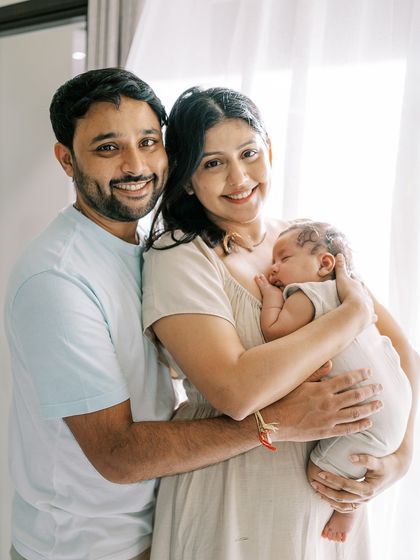 A family with their newborn, standing by a window. The soft, natural light is perfect for these gentle and loving portraits.