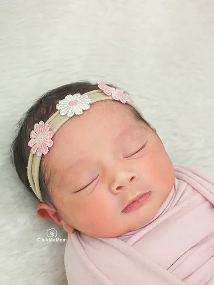 This detailed portrait focuses on the baby's face, adorned with a sweet daisy headband. Her closed eyes and calm expression are so precious.