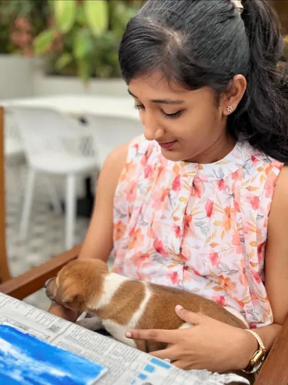 A young girl gently holds a sleeping puppy on her lap while she takes a break from painting.