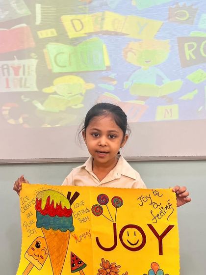A student proudly displays her artwork about the feeling of "Joy" during Literacy Quest Week. We encourage children to express emotions and ideas through both words and art.