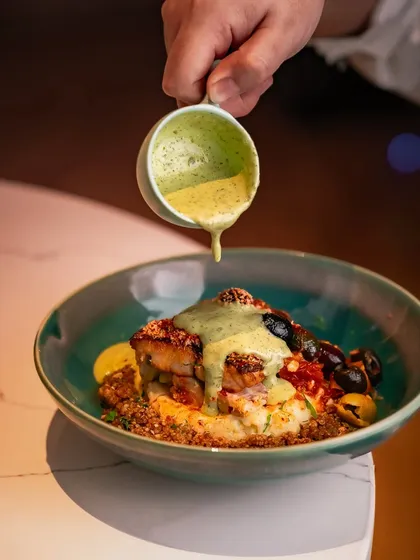 A beautiful seafood dish, with perfectly seared scallops and a rich, creamy sauce being poured over the top. A celebration of culinary creativity.