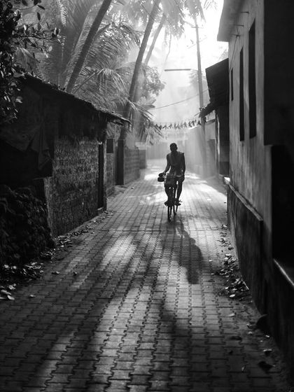 A man cycles down a narrow lane in Gokarna, with sunlight filtering through the palm trees. This 2012 shot captures a simple moment of local life in a timeless monochrome style.