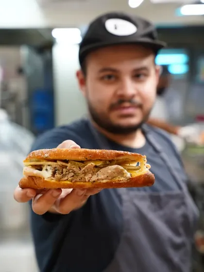 A chef holding up a delicious-looking sandwich for the camera, with the kitchen in the background. This portrait is full of personality and connects the food directly to its creator.
