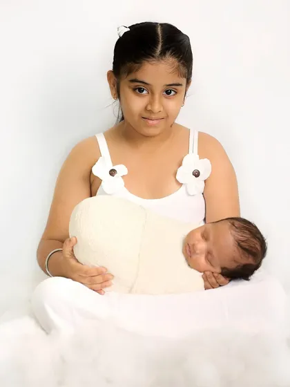 A simple and sweet portrait of an older sister holding her newborn sibling. The all-white theme creates a pure and classic look for this sibling photoshoot.