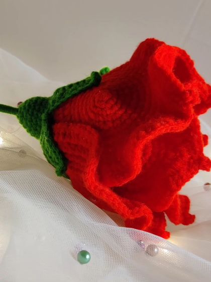 A side view of the crochet rose, showing the detail in the green calyx and the layered petals.