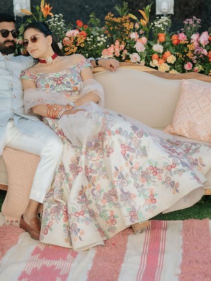 The couple relaxing in their beautifully decorated seating area. The floral backdrop and comfortable furnishings create a perfect spot for them to enjoy their celebration.