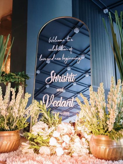 The elegant welcome sign reflects the ballroom's modern ceiling, creating a beautiful contrast with the rustic charm of the floral arrangements in traditional copper pots.