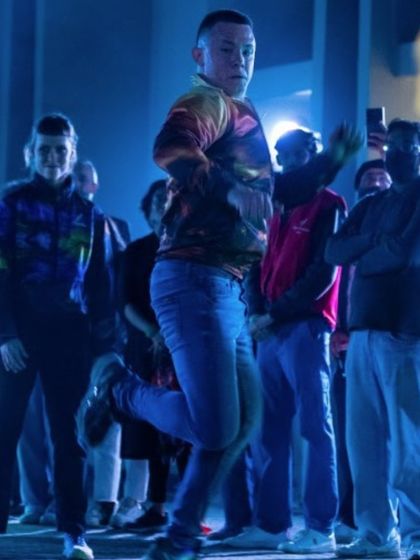 A dancer mid-jump, surrounded by the audience. The "To Da Bone" performance breaks the barrier between stage and spectator, creating a truly immersive experience.