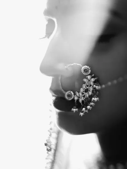 An artistic black and white profile shot of the bride. The high-key lighting and soft focus on her intricate nath create a dreamy and ethereal portrait.