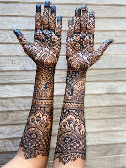 A unique pose showing the back of the hands and arms, covered in a dense pattern of floral, paisley, and elephant motifs.