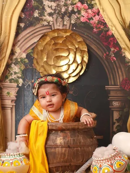 A mischievous little Krishna peeking out from a large pot. This playful pose is a favorite among parents for their baby's Janmashtami photoshoot.