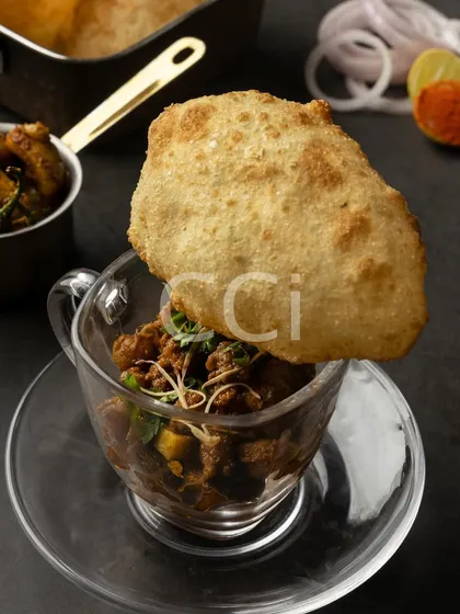 A modern interpretation of a beloved classic, our Chole Bhature. We serve the spiced chickpea curry in a glass cup, topped with a single, perfectly puffed bhatura, transforming a traditional dish into a chic, single-serving experience.