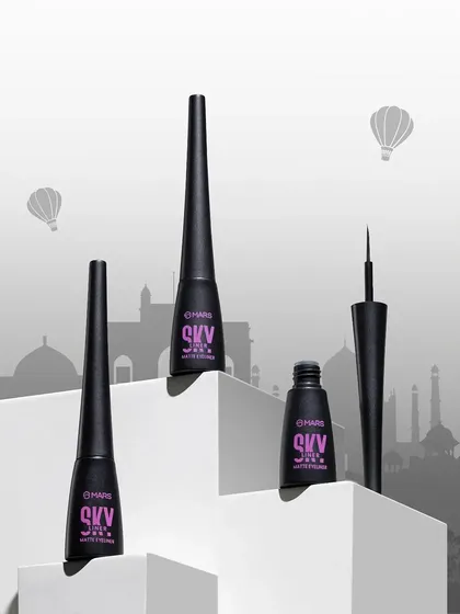 A conceptual shot for "Skyliner" eyeliner, where the products are arranged on white blocks against a silhouette of a city skyline, cleverly tying the product to its name.