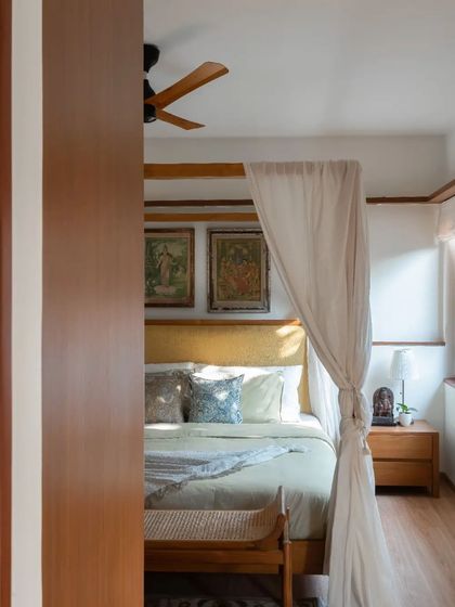 A custom teak four-poster bed, designed to be a statement piece. The fabric headboard and sheer curtains add a touch of softness and luxury.