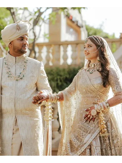 A classic couple portrait showcasing their stunning wedding day ensembles. The groom's layered pearl and emerald necklace perfectly complements the bride's choker, demonstrating a thoughtful approach to coordinated accessorizing.