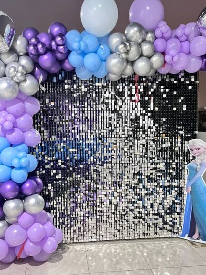 The main backdrop for the Frozen party, featuring an arch of purple, blue, and silver balloons over a shimmering silver sequin wall with an Elsa cutout.