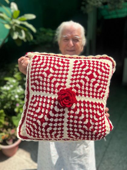 A classic and elegant cushion cover in red and cream, featuring a beautiful texture and a central crocheted rose for a touch of romance.