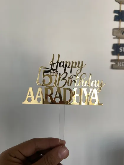 Another angle of the "Happy 5th Birthday AARADHYA" topper, held up to show its size and the beautiful reflection of the gold acrylic.