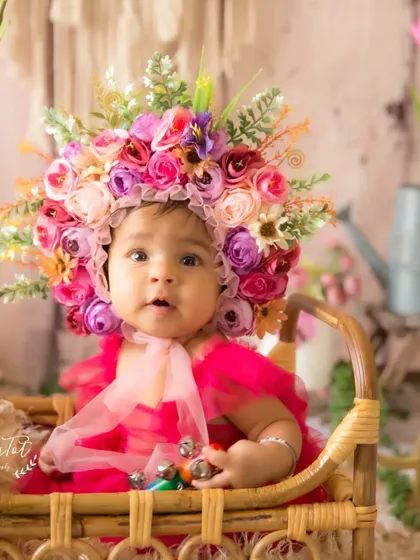 Holding a little rattle, this baby is all smiles in her vibrant pink dress and floral bonnet during her half-birthday photoshoot.