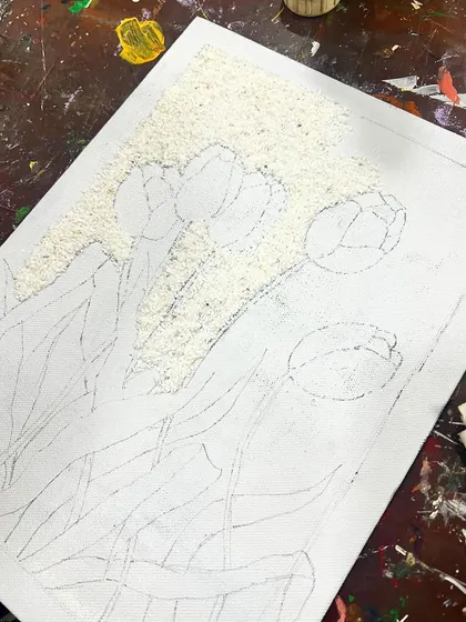 The beginning stages of a mixed-media piece, with rice being glued to the canvas to create a unique textured background.