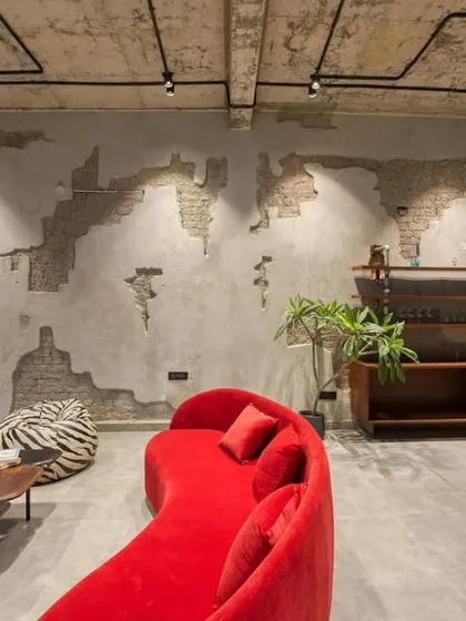 This industrial-style lounge area features exposed brick and concrete walls, a bright red curved sofa, and a foosball table, creating a fun and edgy entertainment space.