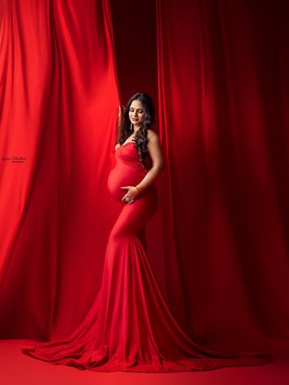 A quiet moment of reflection. The mom-to-be cradles her bump, surrounded by the warmth and passion of the color red.